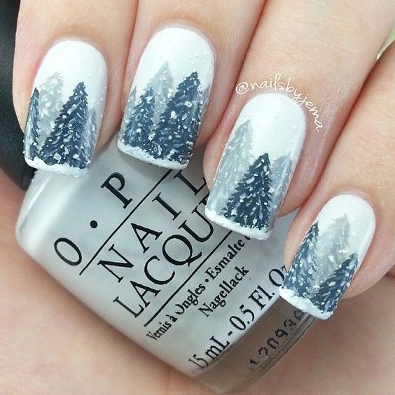 Uñas pintadas con base blanca y dibujos de pinos navideños en tonos grises; diseños de manicuras navideñas