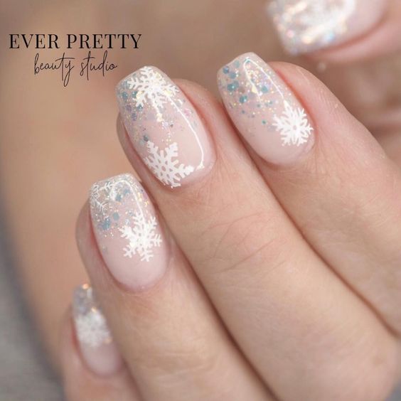 Uñas en tono rosa palo con decoración de copos de nieve en blanco y gris; diseños de manicuras navideñas