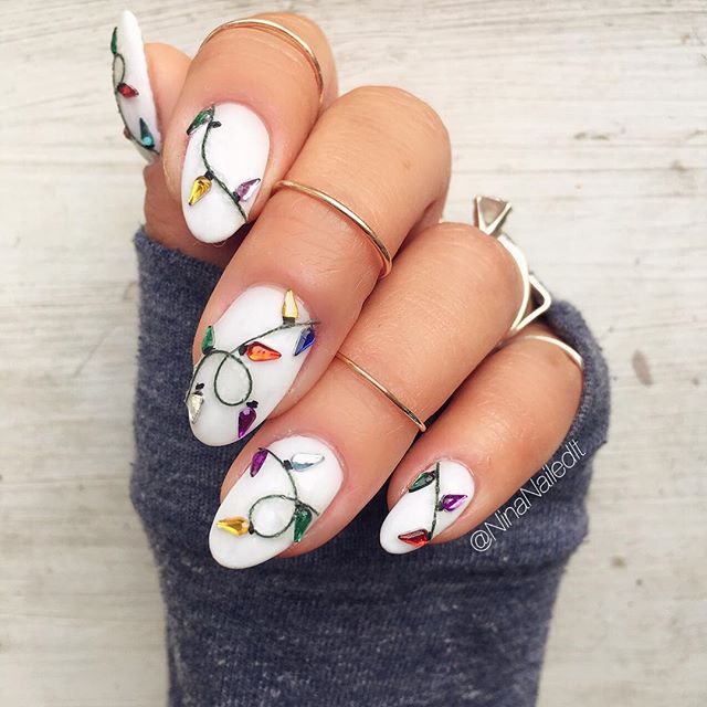 Uñas pintadas en blanco con un diseño de luces navideñas de colores; diseños de manicuras navideñas