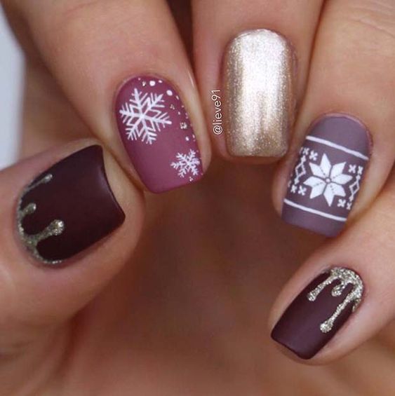 Uñas en tonos morados con decoraciones de copos navideños en blanco; diseños de manicuras navideñas