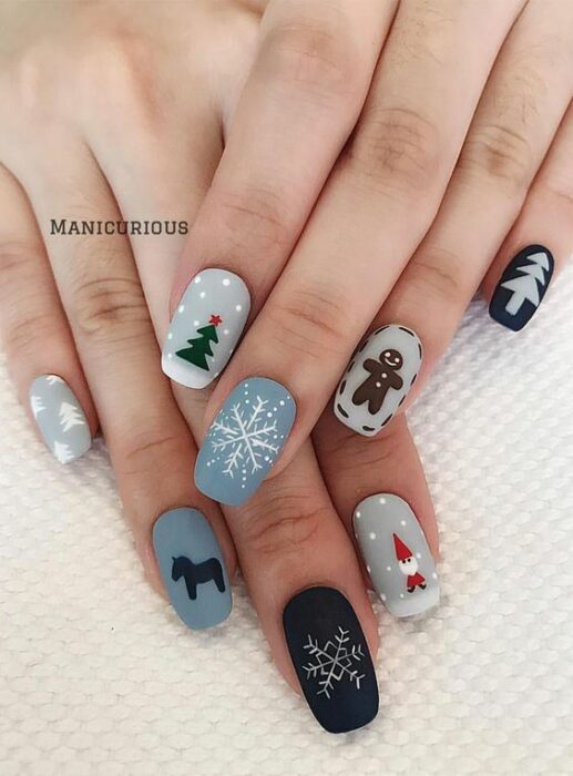 Uñas en base gris y azul decoradas con motivos navideños; diseños de manicuras navideñas