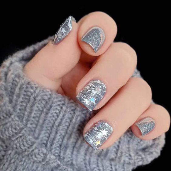 Uñas en base plata con destellos blancos en forma de estrella; diseños de manicuras navideñas