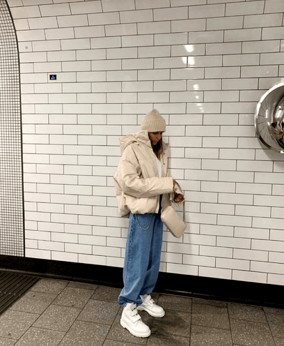 chica de cabello castaño usando un beanie gorro beige, chamarra puffer jacket beige, jeans holgados, botines blancos de suela gruesa