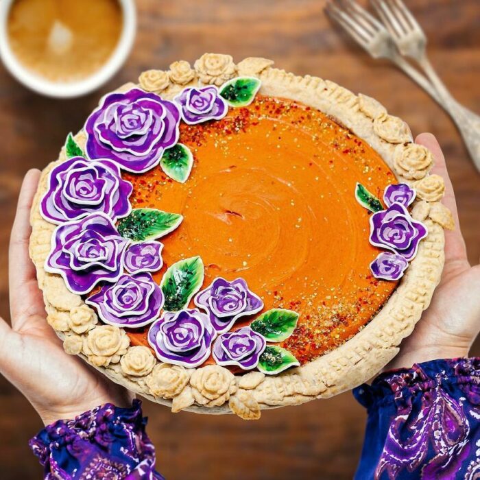 Pay de calabaza adornado con flores moradas y hojas verdes