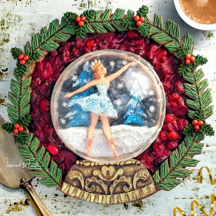 Pay decorado con una bailarina en una bola de nieve, adornado con ramas comestibles de pino