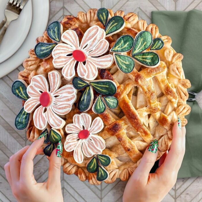 Pay con cobertura crujiente adornado con flores comestibles blancas y hojas verdes