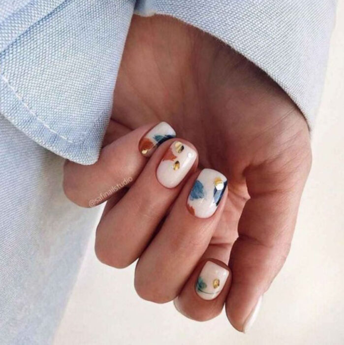 Manicura con fondo beige y detalles en azul, naranja y amarillo