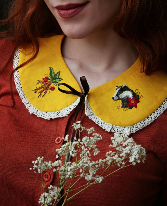 Little pin studio crea bonitos cuellos bordados de Halloween para vestidos y blusas; diseño de Hufflepuff, mandrágora, tejón sobre tela amarilla; mujer pelirroja con blusa anaranjada sonriendo