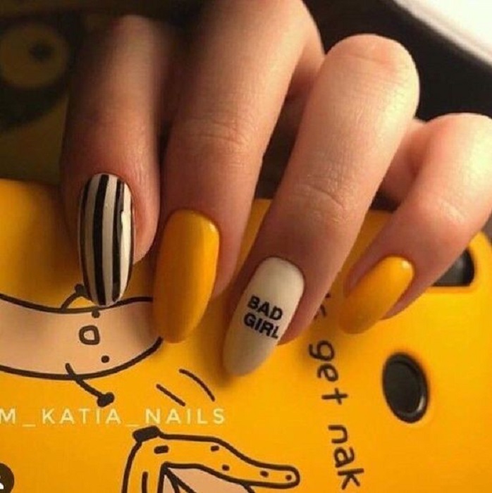 Manicura en color mostaza con variación en blanco y negro además de una pequeña frase