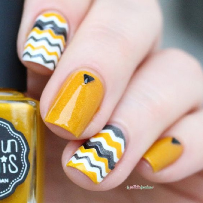Manicura en color mostaza con una piedrita y diseño de líneas en otros colores