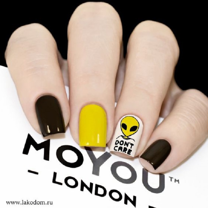 Manicura en color mostaza con un diseño de un ovni en el dedo anual y color negro en otros dedos