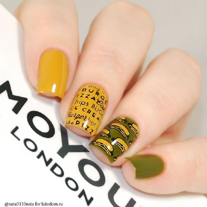 Manicura en color mostaza con diseño de letras en un dedo, tono verde olivo y hot dogs dibujados