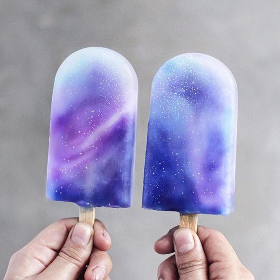 Dos manos sosteniendo paletas de hielo con efecto de galaxia
