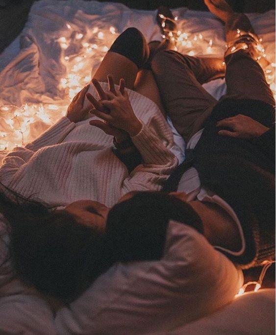 Pareja acostada en el piso con sus cabezas apoyadas en almohadas blancas rodeados de luces navideñas amarillas