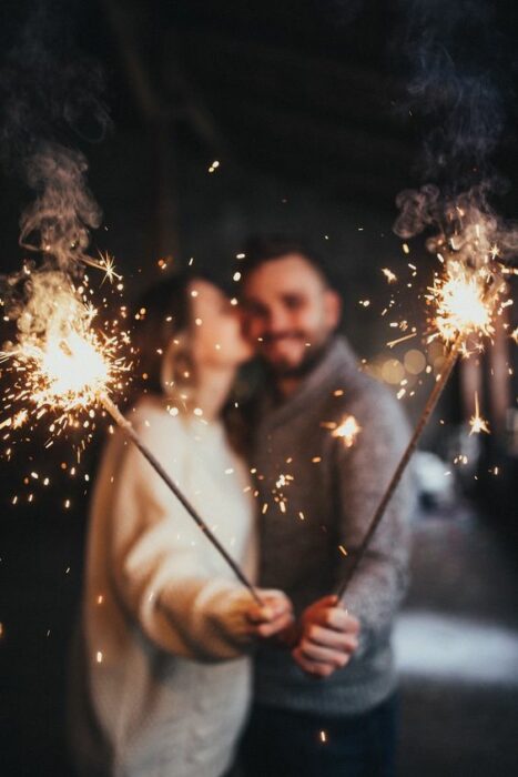 Pareja desenfocada enciende luces de bengala grandes frente a cámara fotográfica