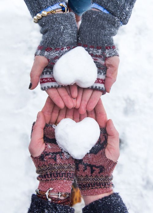 Manos de una pareja unidas en medio de foro ambas con guantes navideños con dos corazones de nieve
