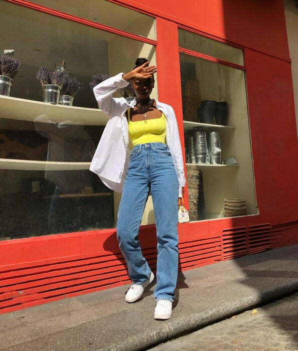 Chica usando jeans y top amarillo con camisa blanca sobre él