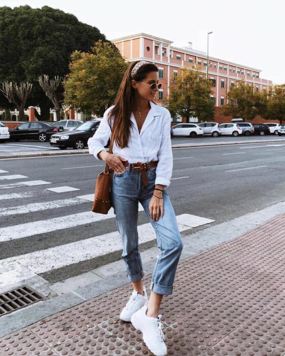 Chica usando una camisa blanca con botones y jeans, acompañada de tenis