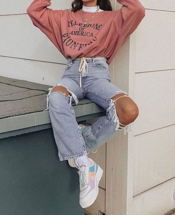 Chica usando mom jeans rasgados, tenis y blusa de cuello alto blanca con sudadera oversized rosa palo