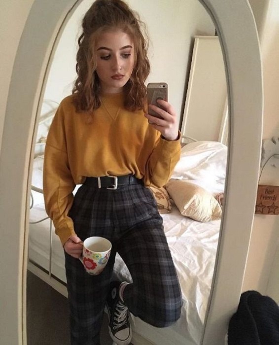 Chica usando pantalón de estampado tartán, converse negros y sudadera color mostaza