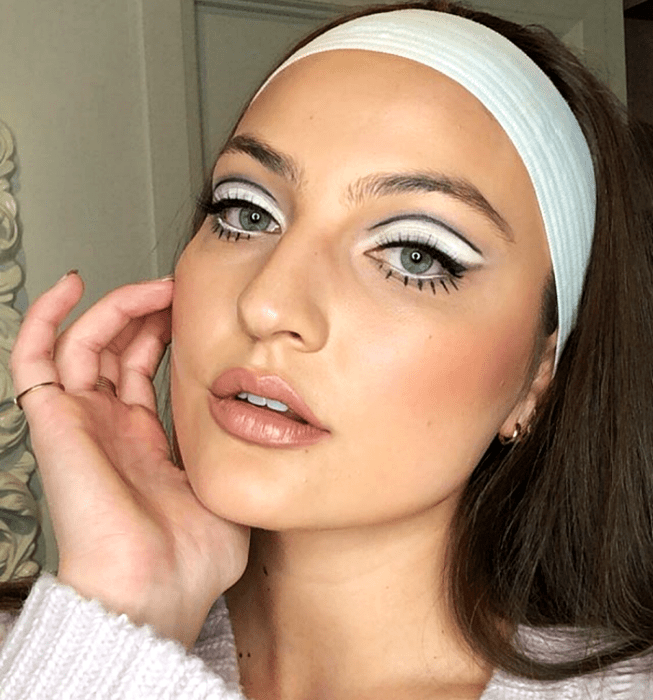 chica de cabello castaño usando maquillaje retro con sombras blancas y delineado gráfico negro