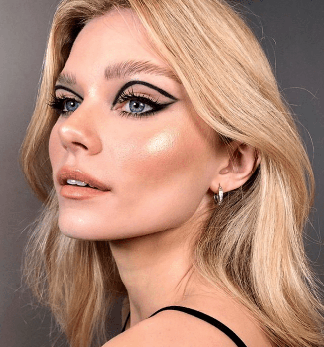 chica rubia usando delineado negro, sombras nude y labial naranja