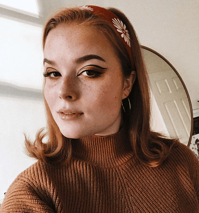 chica pelirroja usando maquillaje con delineado negro y sombras en tonos cálidos