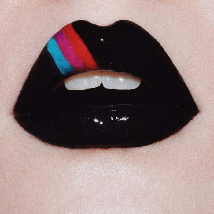 Maquillaje artístico de labios por maquilladora Tatiana Rose; boca con labial negro y gloss, adornados con líneas azules, rosas y rojas