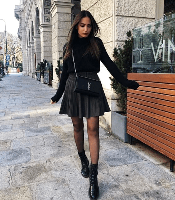 chica con cabello largo castaño usando un suéter negro, minifalda amplia, medias oscuras y botines