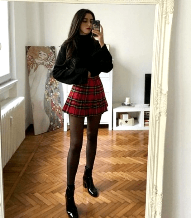 chica con suéter negro, falda de tablones roja con negra, medias negras y botines