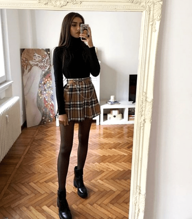 chica con suéter de cuello alto negro, falda de tablones, medias negras y botines negros