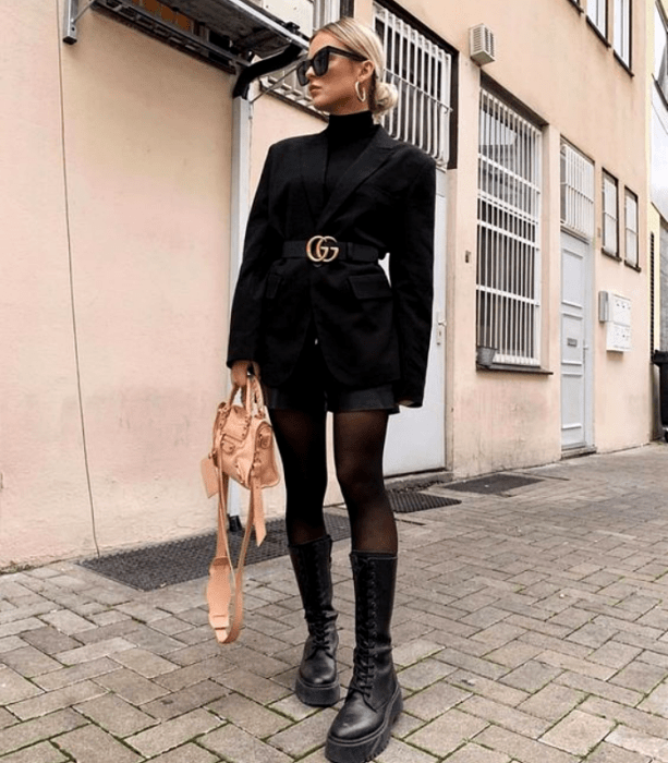 chica rubia con gafas de sol, abrigo negro con cinturón, minifalda negra, medias negras y botas gruesas de cuero