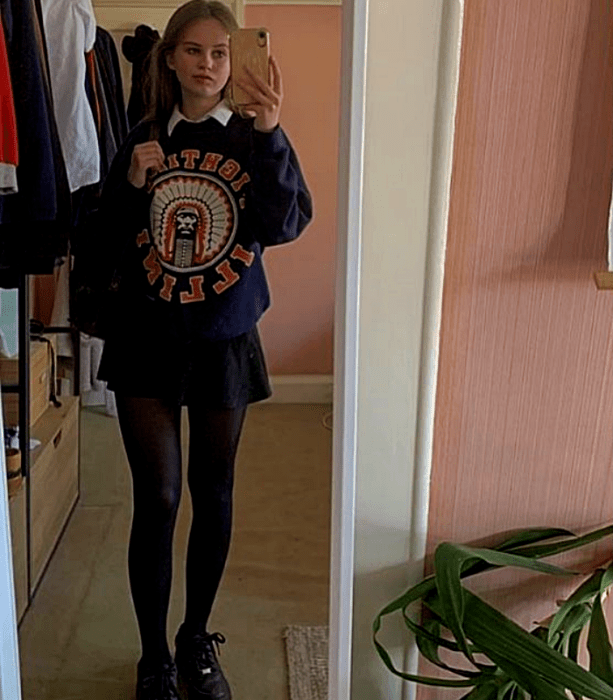 chica rubia con sudadera estampada, minifalda negra, medias negras y tenis deportivos
