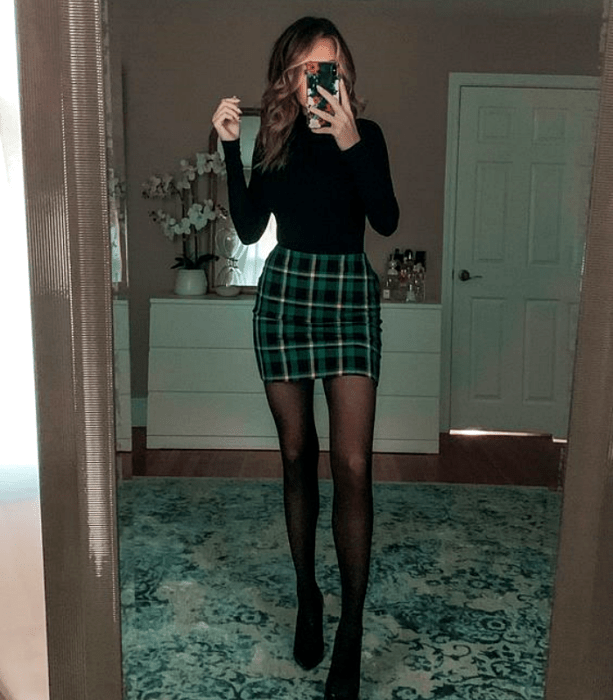 chica con camiseta de manga larga con cuello alto, minifalda verde de cuadros, medias negras y botines de cuero
