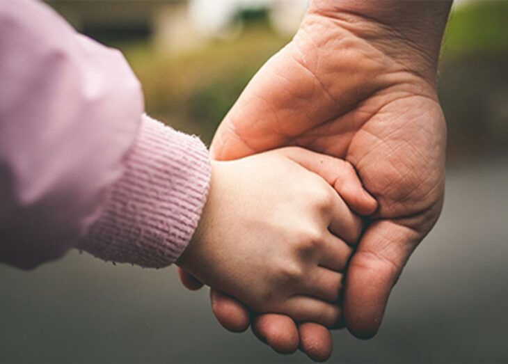 Mano de hombre sujetando la manita de una niña con suéter rosa