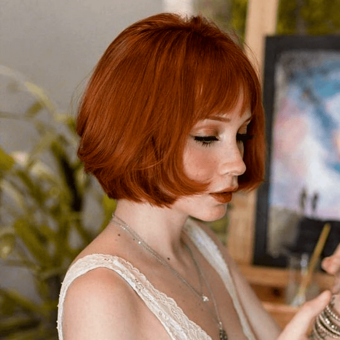 chica pelirroja con corte estilo french bob, bob francés, usando una blusa beige de encaje de tirantes