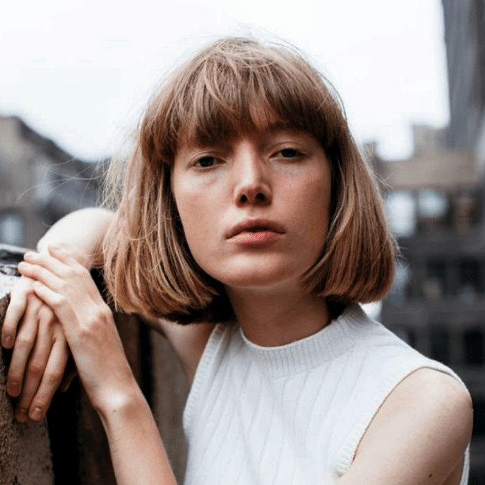 chica rubia usando un corte estilo french bob, bob francés, con un suéter sin mangas de cuello alto color beige