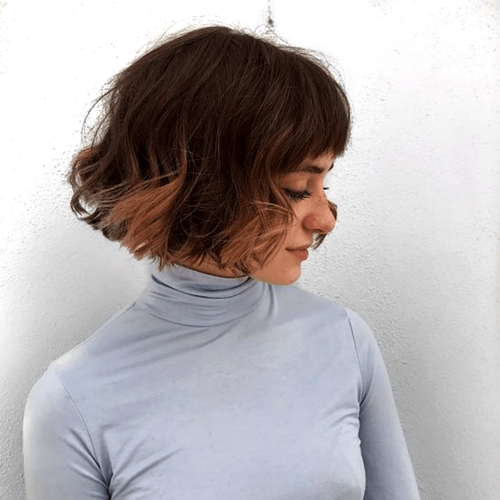 chica de cabello castaño con luces con corte de cabello estilo french bob, bob francés, y top gris de manga larga y cuello alto