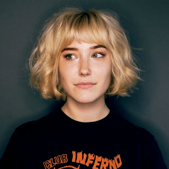 chica rubia con corte de cabello estilo french bob, bob francés, usando una camiseta negra con letras naranjas