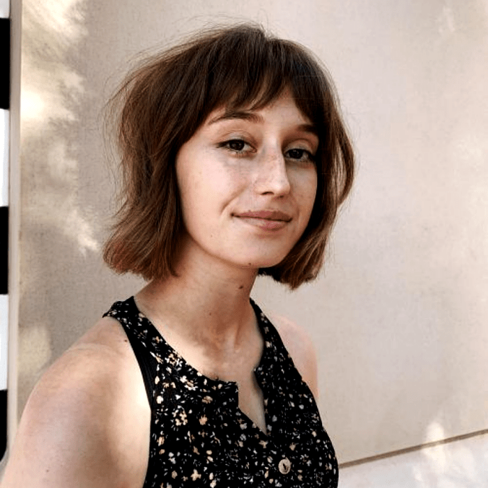 chica de cabello castaño claro con corte de cabello estilo bob francés, french bob, y un top negro con flores de tirantes