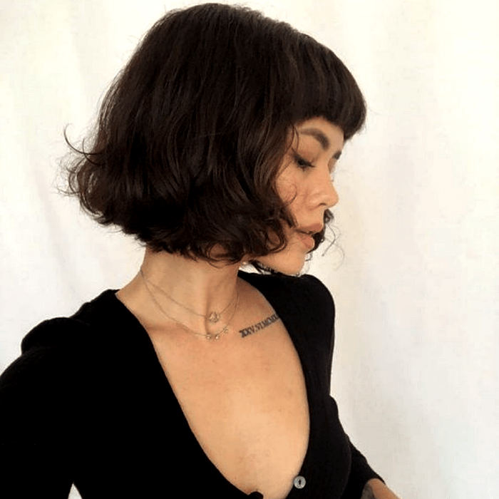 chica de cabello castaño oscuro usando corte de cabello estilo french bob, bob francés, top negro de manga larga con cuello en V