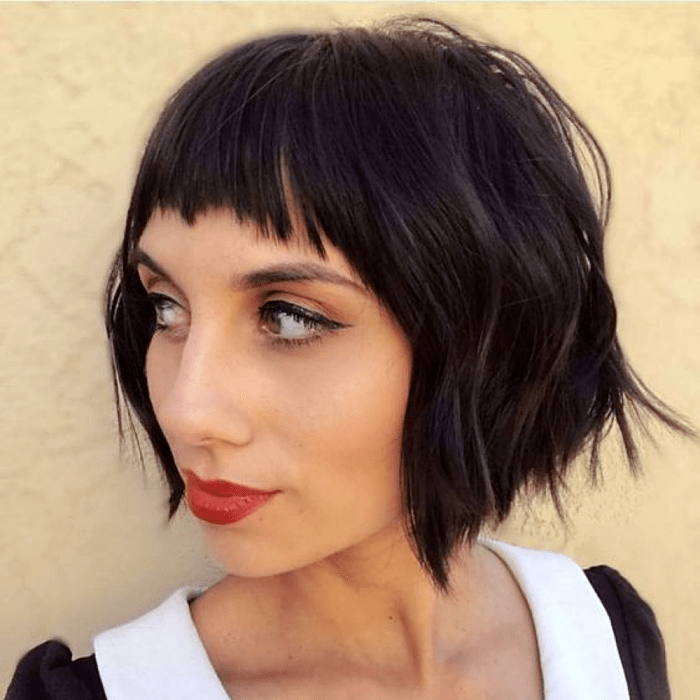 chica de cabello oscuro con corte estilo french bob, bob francés, usando lipstick rojo y top negro con cuello blanco en V