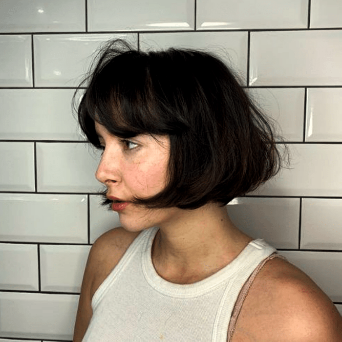 chica de cabello oscuro usando un corte de cabello estilo french bob, bob francés con un top blanco de tirantes