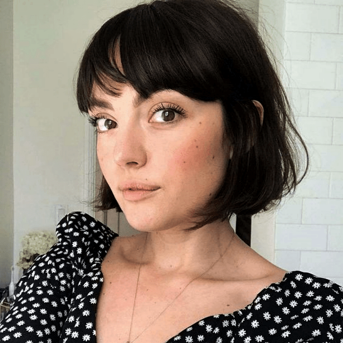 chica de cabello castaño usando un corte estilo bob francés, french bob con un top negro de flores blancas