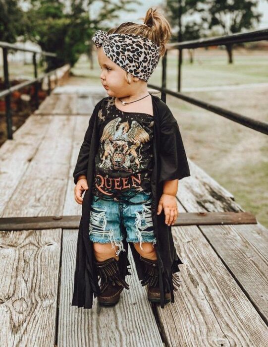 Bebé rubia con banda de animal print en la cabeza con short de mezclilla, botas negras altas, blusa rockera y kimono negro