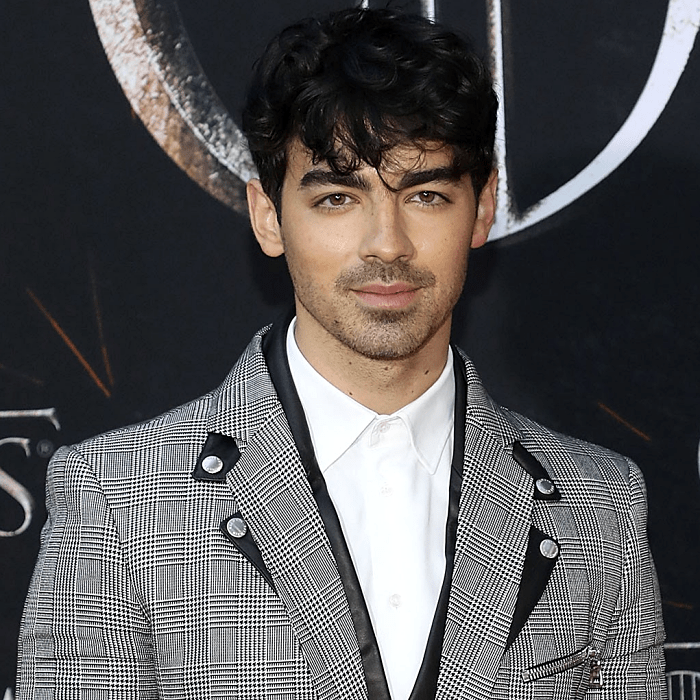 joe jonas usando una camisa polo blanca, saco gris de cuadros con aplicaciones de cuero
