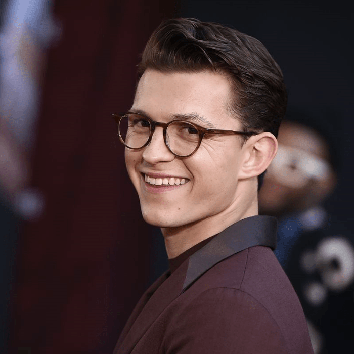 tom holland usando lentes de contorno café, camisa de vestir guinda y saco guinda