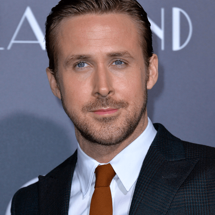 ryan gosling usando una camisa de vestir blanca con corbata naranja y saco negro con cuadros y textura