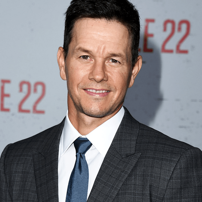 mark wahlberg usando una corbata azul, camisa de vestir blanca y saco gris oscuro de cuadros