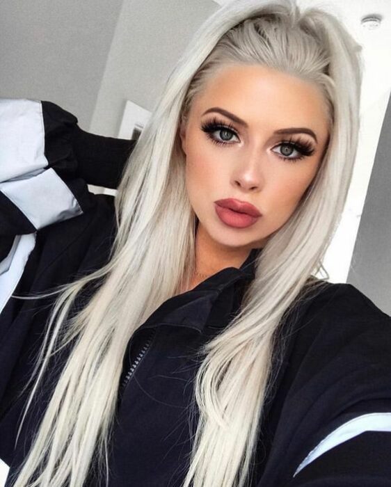 Chica de ojos grises y labios gruesos rosas vistiendo una sudadera negra con franjas blancas en las mangas y cabello largo en media coleta en tono 'icy blonde'